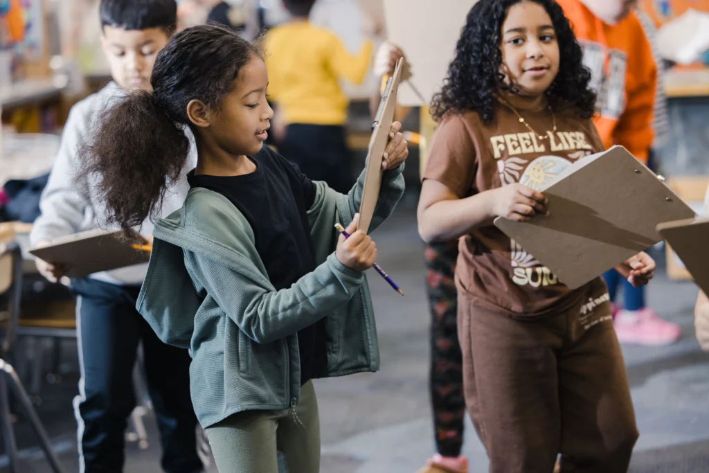 Second graders look at clipboards as they walk around their classroom