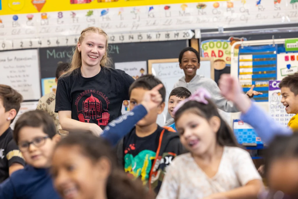 A college student surrounded by second graders smiles